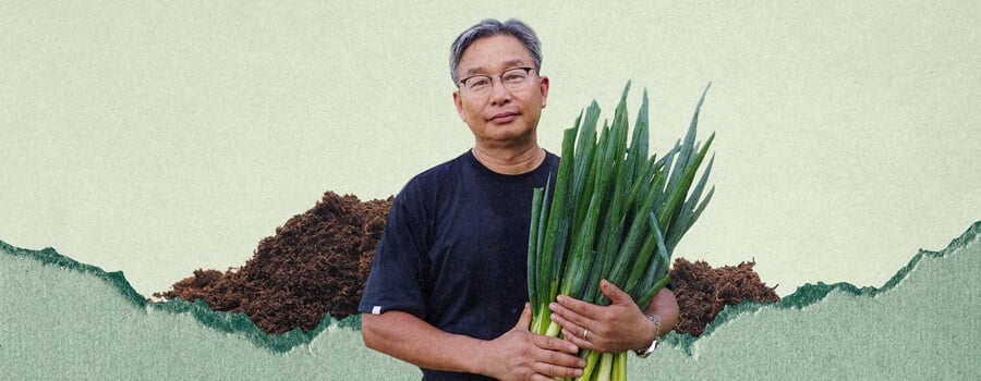 Un uomo di nome Youngsang Cho tiene in mano un mazzo di cipollotti. Si trova davanti a un mucchio di terra.