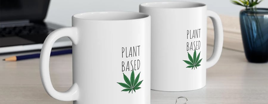 Due tazze bianche con le parole "Plant Based" e una foglia di marijuana verde stampate.