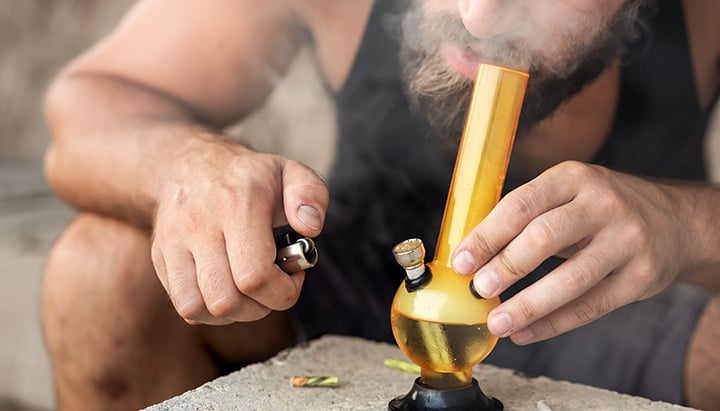 Persona che fuma hashish da una pipa di vetro, espirando fumo denso.